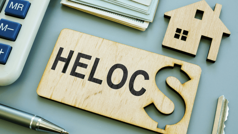 Wooden sign with the word HELOC next to a small house figurine and calculator representing a Home Equity Line of Credit