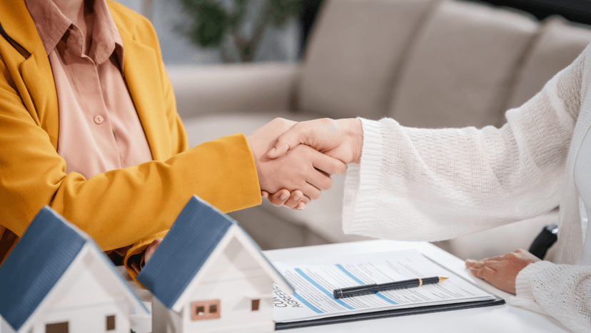 Homeowner and consultant shaking hands over property documents and houses